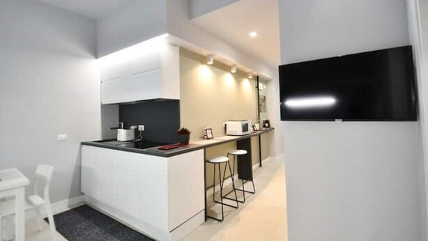 A modern kitchen with a central island, bar stools, and a flat-screen TV mounted on the wall. - SIMONA's apartment in Rome a stone's throw from St. Peter's (ROMA)
