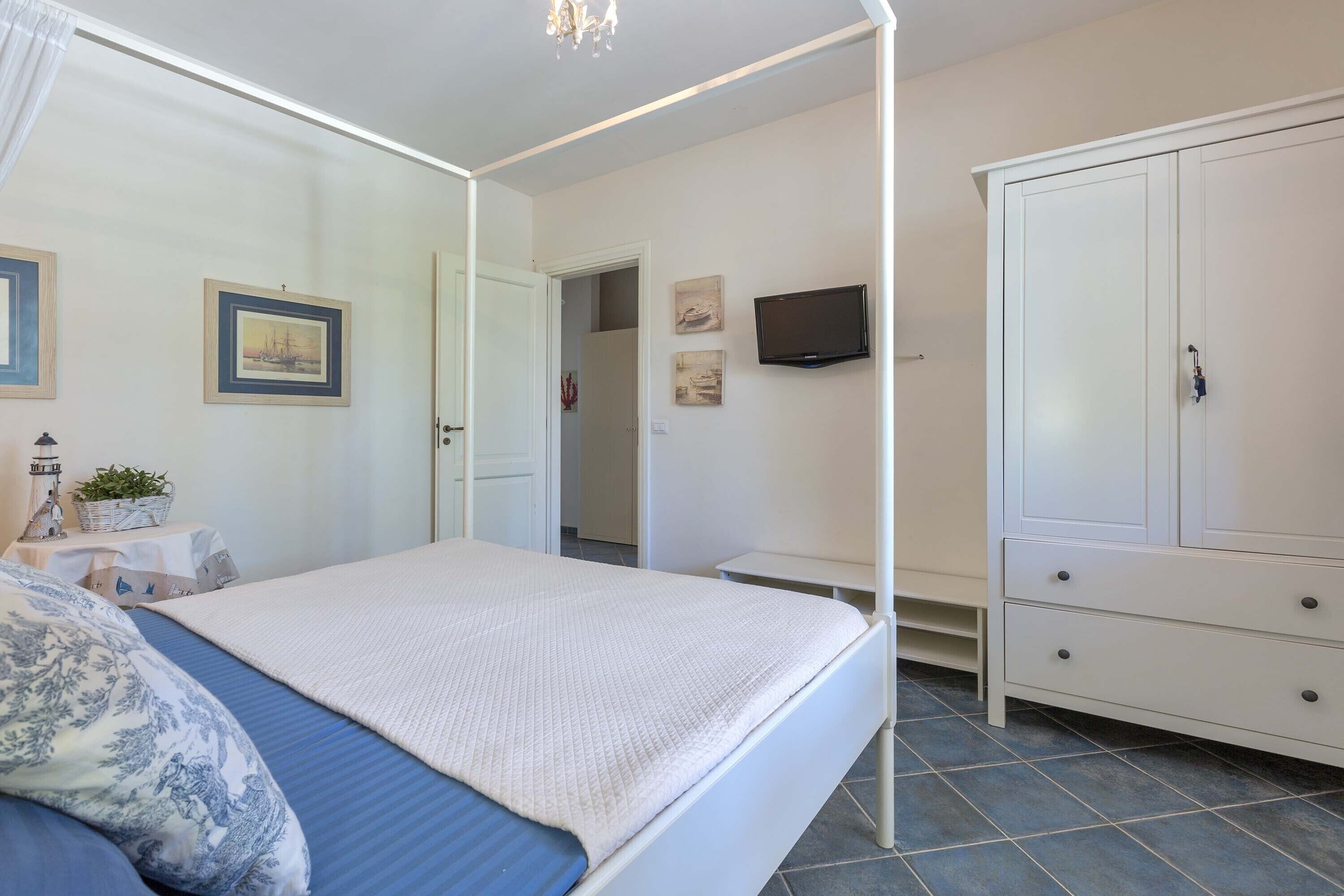 Ein Schlafzimmer mit einem Bett, einem Kleiderschrank, einem Fernseher und einer Tür zu einem weiteren Raum.