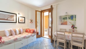 Una habitación acogedora con sofá, una mesa de comedor con sillas, una pequeña cocina y una puerta que da a un espacio exterior.