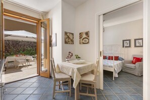Une pièce comprenant un lit, une table à manger avec des chaises et une petite table sur laquelle est posé un vase. Deux tableaux encadrés ornent le mur.
