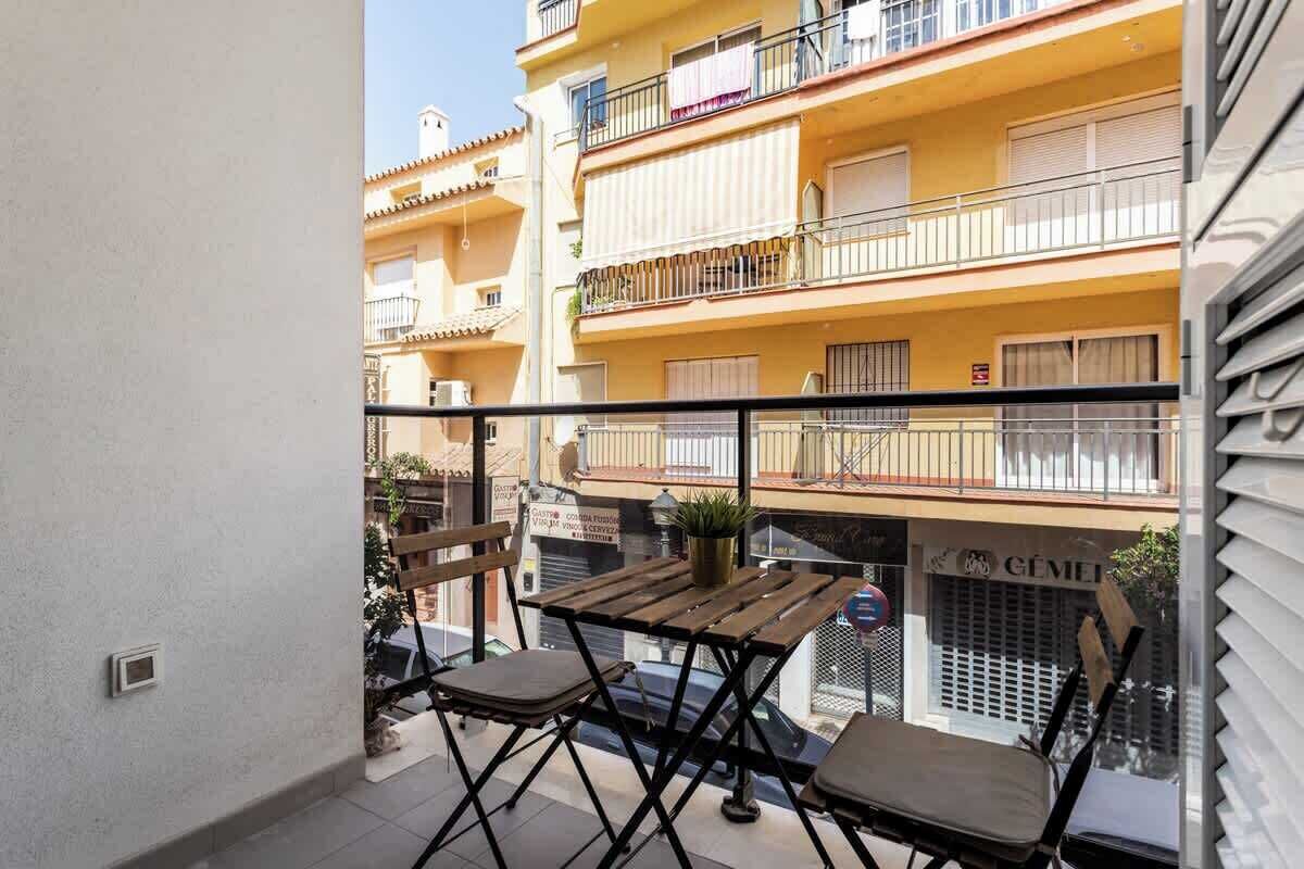 En balkon med et træbord og to stole, med udsigt over en gul bygning med balkoner.