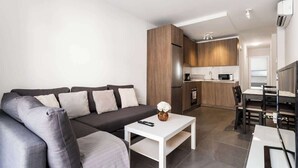 A modern living room with a grey sofa, a white coffee table, and a kitchen area with wooden cabinets and a microwave.