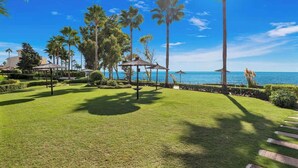 A well-maintained lawn with palm trees and a gazebo, overlooking a clear blue sea.