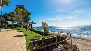 A coastal walkway with a wooden fence, a thatched-roof structure, and a view of the ocean.