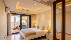 A modern hotel room with a large bed, bedside tables, and a view of the sea through an open door.