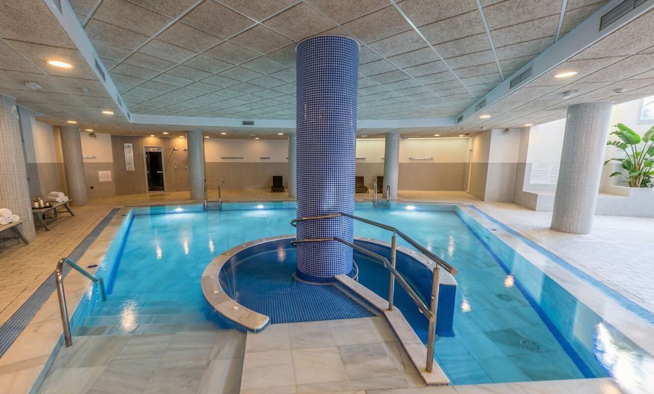 Une piscine intérieure dotée d’une colonne centrale, de murs carrelés et d’un sol carrelé.