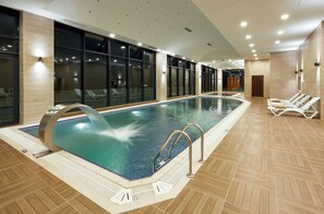 Ein Innenpool mit klarem Wasser, gefliestem Boden und einer Liegebereich mit Sonnenliegen.