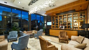 Ein moderner Lounge-Bereich mit Sofas und Sesseln, eine Bar mit Flaschenregalen und große Fenster mit Blick auf die Stadt.