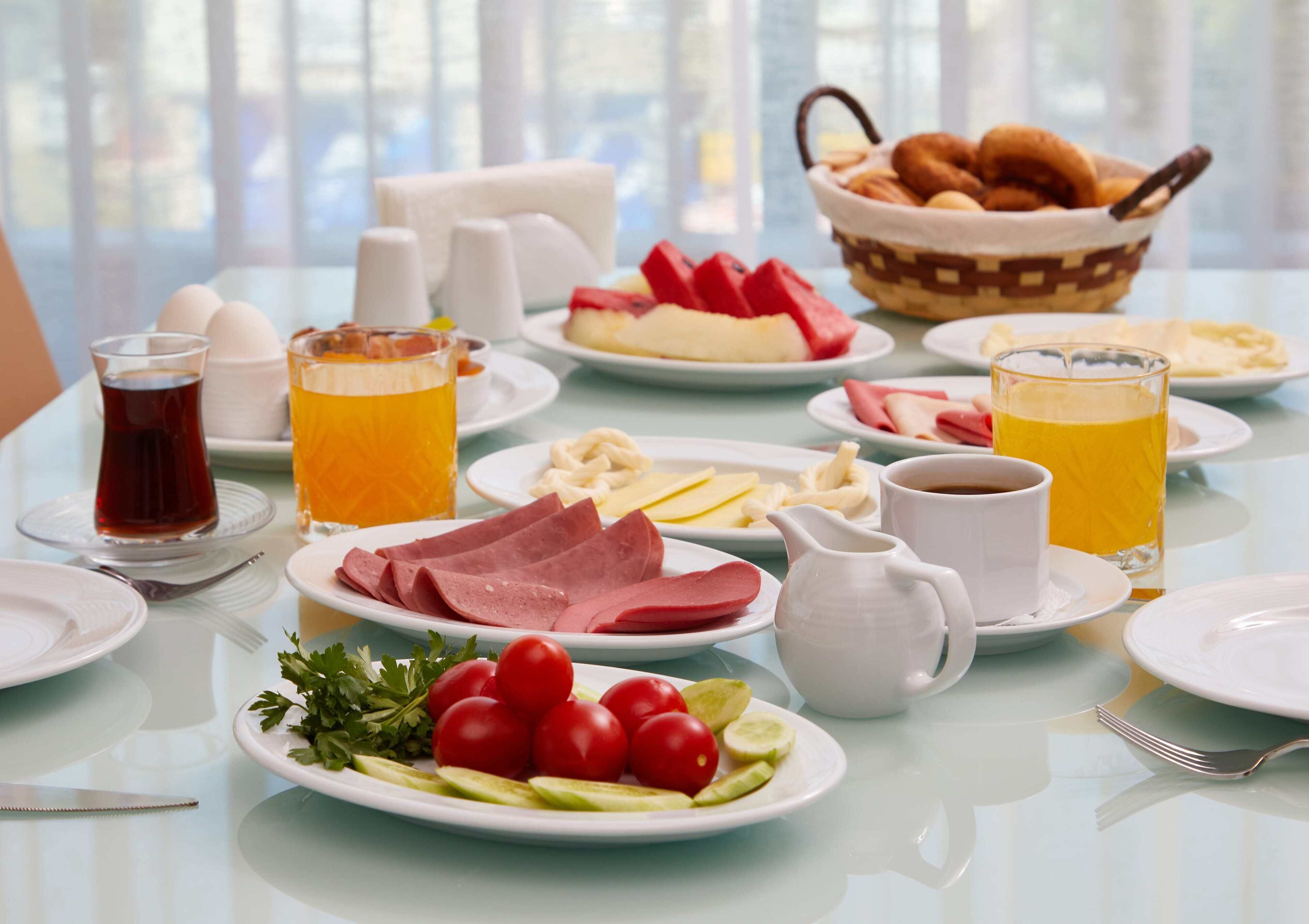 A breakfast table with plates of food, glasses of juice, and a basket of pastries.
