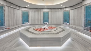 Ein luxuriöses Badezimmer mit einer zentralen, runden Marmorplattform, mehreren Waschbecken und dekorativen, blauen Mosaikfliesen.