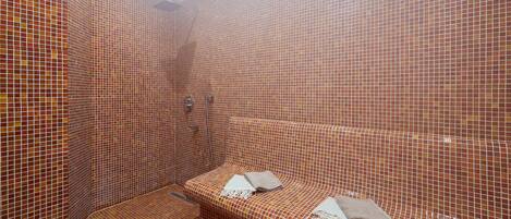 Un baño pequeño con paredes y piso de azulejos, una banca y un perchero.