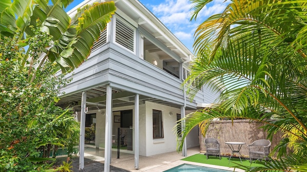 A two-story house with a covered patio, a swimming pool, and lush tropical vegetation.