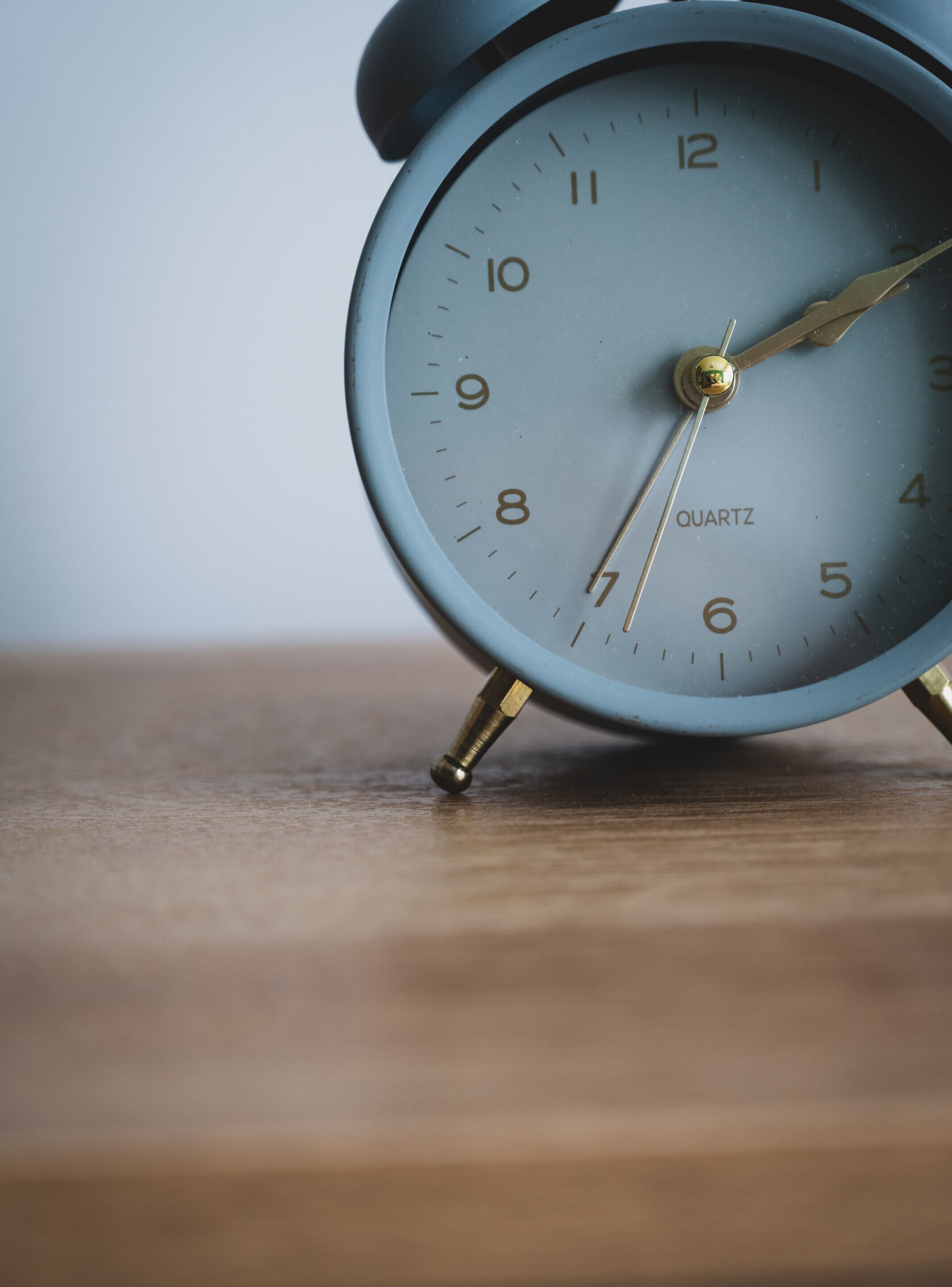 A close-up of a blue quartz alarm clock with a gold-tone pendulum, placed on a wooden surface.