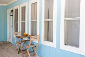 A porch with a wooden table and chairs, a small flower arrangement, and a window with a white frame. - Charming 1-bedroom at Exuma Yacht Club (George Town)