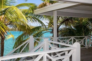 A white wooden deck with a white railing overlooking a turquoise ocean, surrounded by palm trees. - Charming 1-bedroom at Exuma Yacht Club (George Town)