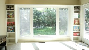 A room with a large window, a bookshelf with board games, and a radiator.