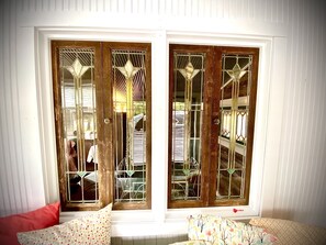 Una habitación con dos ventanas grandes de madera y vidrios decorativos, y una pared blanca.