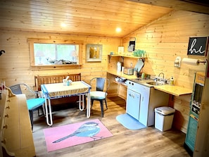 Una cocina acogedora de estilo cabaña con paredes de madera, una mesa de comedor, sillas, un refrigerador pequeño y un lavamanos.