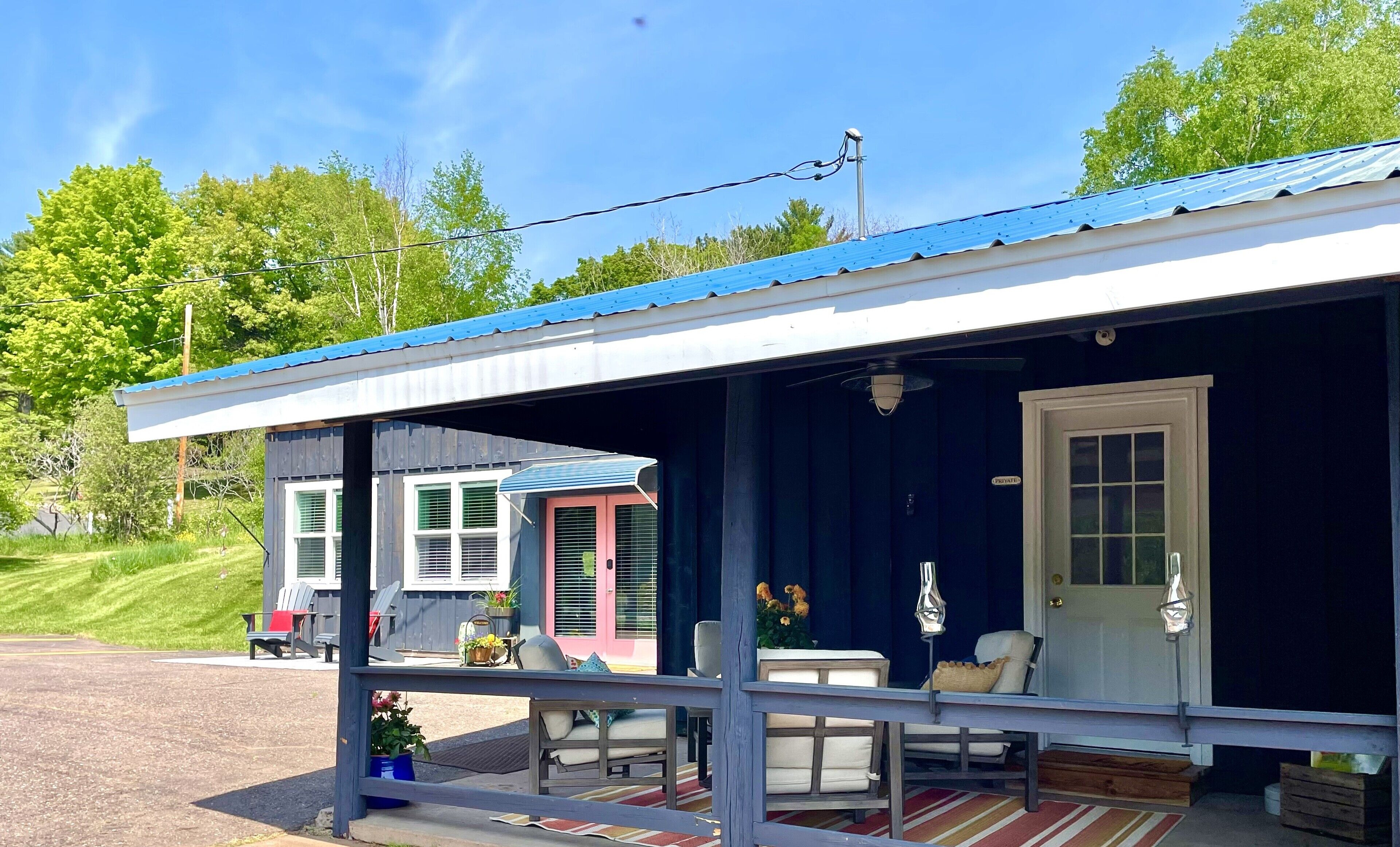 Ein kleines, eingeschossiges Gebäude mit blauem Dach und einer Veranda mit Sitzgelegenheiten.