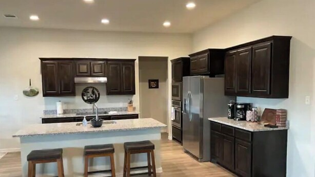 A modern kitchen with dark wooden cabinets, a stainless steel refrigerator, and a granite countertop. - Brazos River Ranch near PK & Rocker B Ranch  (Mineral Wells)