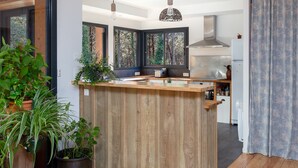A modern kitchen with a wooden island, large windows, and a view of the forest. - Wooden House With Heated Pool, Fiber Internet and View Into Forest (Moliets-et-Maa)