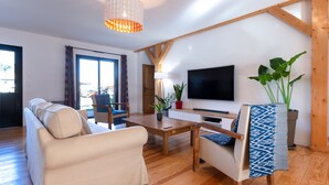 A modern living room with a sofa, armchairs, a coffee table, a TV, and wooden beams on the ceiling. - Wooden House With Heated Pool, Fiber Internet and View Into Forest (Moliets-et-Maa)