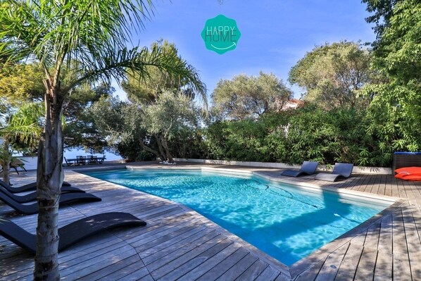A swimming pool with lounge chairs and a wooden deck, surrounded by trees.