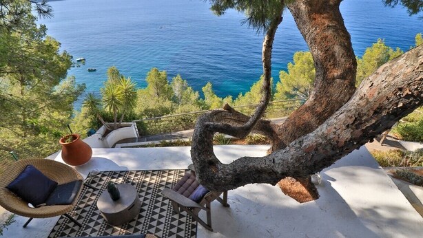 Una terraza con mobiliario exterior, un árbol grande y vista al mar.