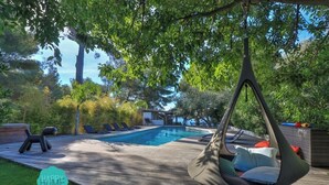 Una terraza de madera con una hamaca colgante, una piscina y sillones de descanso.