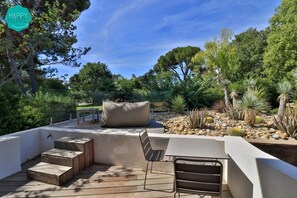 An outdoor patio with a seating area, steps leading up to a white wall, and a variety of plants and cacti.