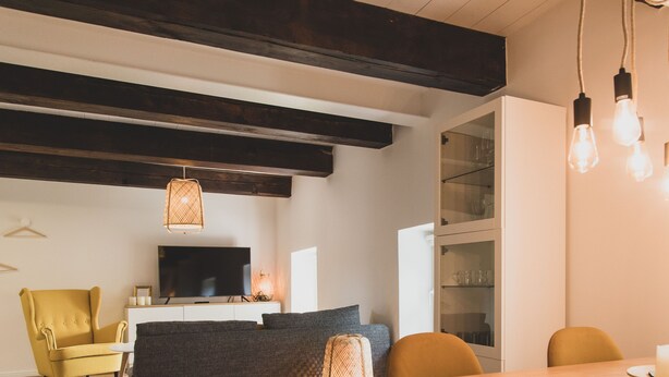 Ein modernes Wohnzimmer mit einer Couch, einem gelben Sessel, einem Esstisch mit Stühlen, einem Flachbildfernseher und einer Vitrine.