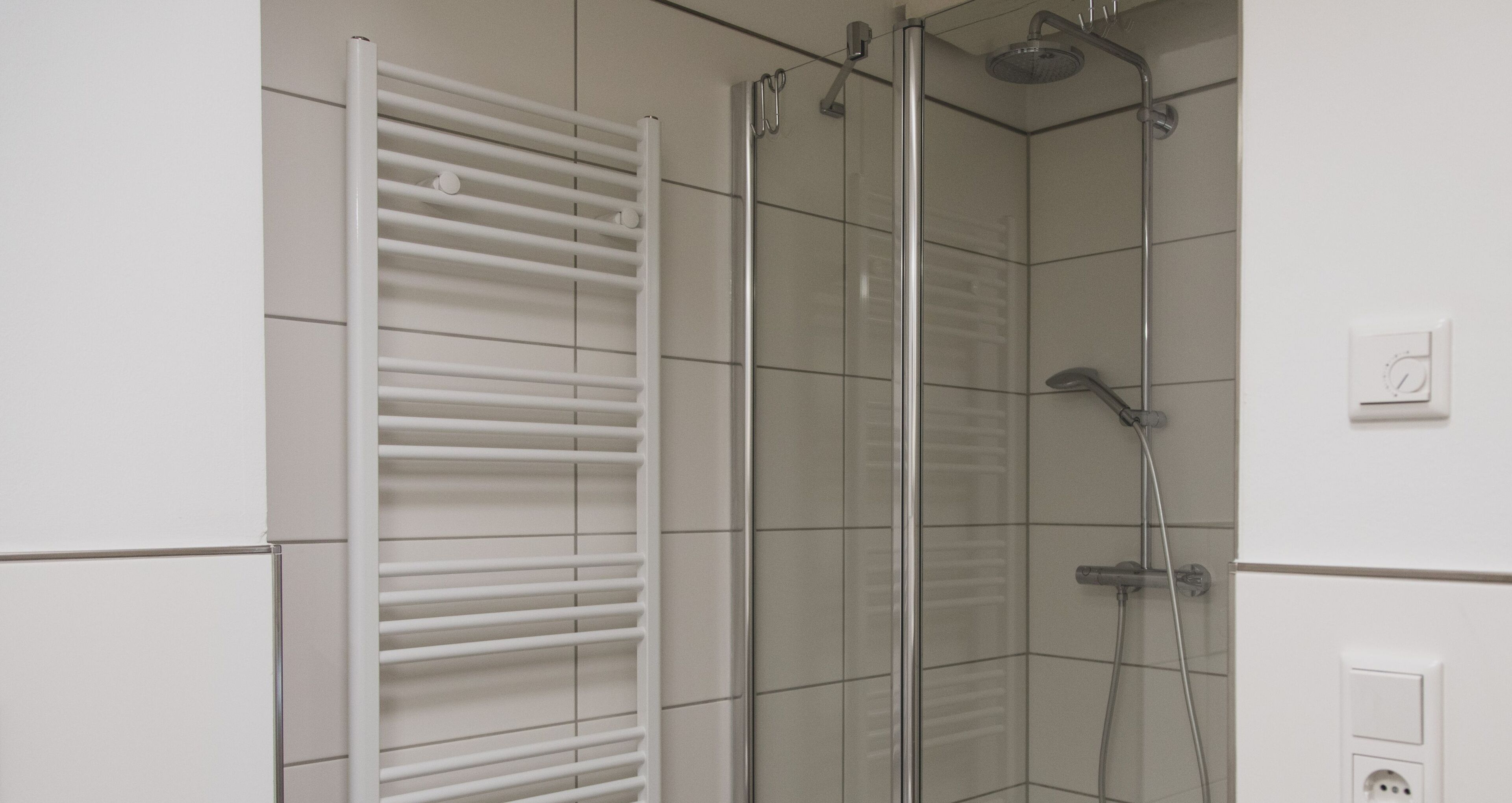 A shower with a glass door, a white towel rack, and a wall-mounted control panel.