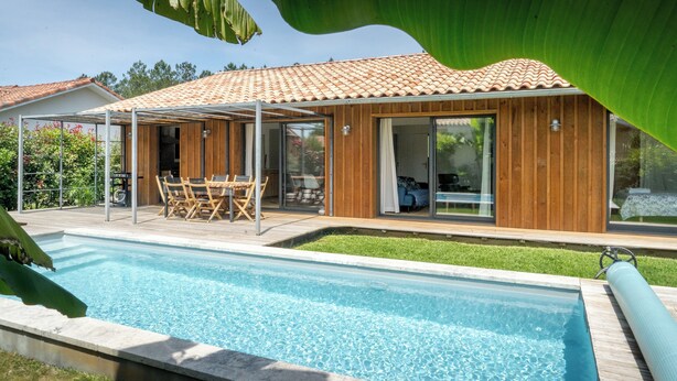 Ein modernes Haus mit Swimmingpool, Holzfassade und einer überdachten Terrasse.
