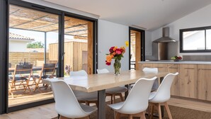 Eine moderne Küche mit einem Holztisch und weißen Stühlen, einer Blumenvase und Blick auf die Terrasse.