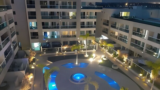 A multi-level building with a central courtyard featuring a circular water feature and surrounding greenery. - Brisas do Lago - apartamento 5 (Brasília)