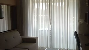 A room with a sofa, a TV, and sheer curtains. - Brisas do Lago - apartamento 5 (Brasília)