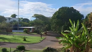 A grassy area with a paved path, a building with a flat roof, and a tall communication tower. - Brisas do Lago - apartamento 5 (Brasília)