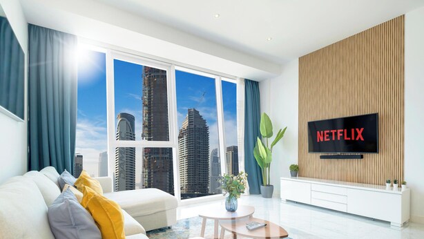 A modern living room with a large window, a sofa, a coffee table, a TV, and a plant. - LUX The Pad Executive Suite 2 (Dubai)
