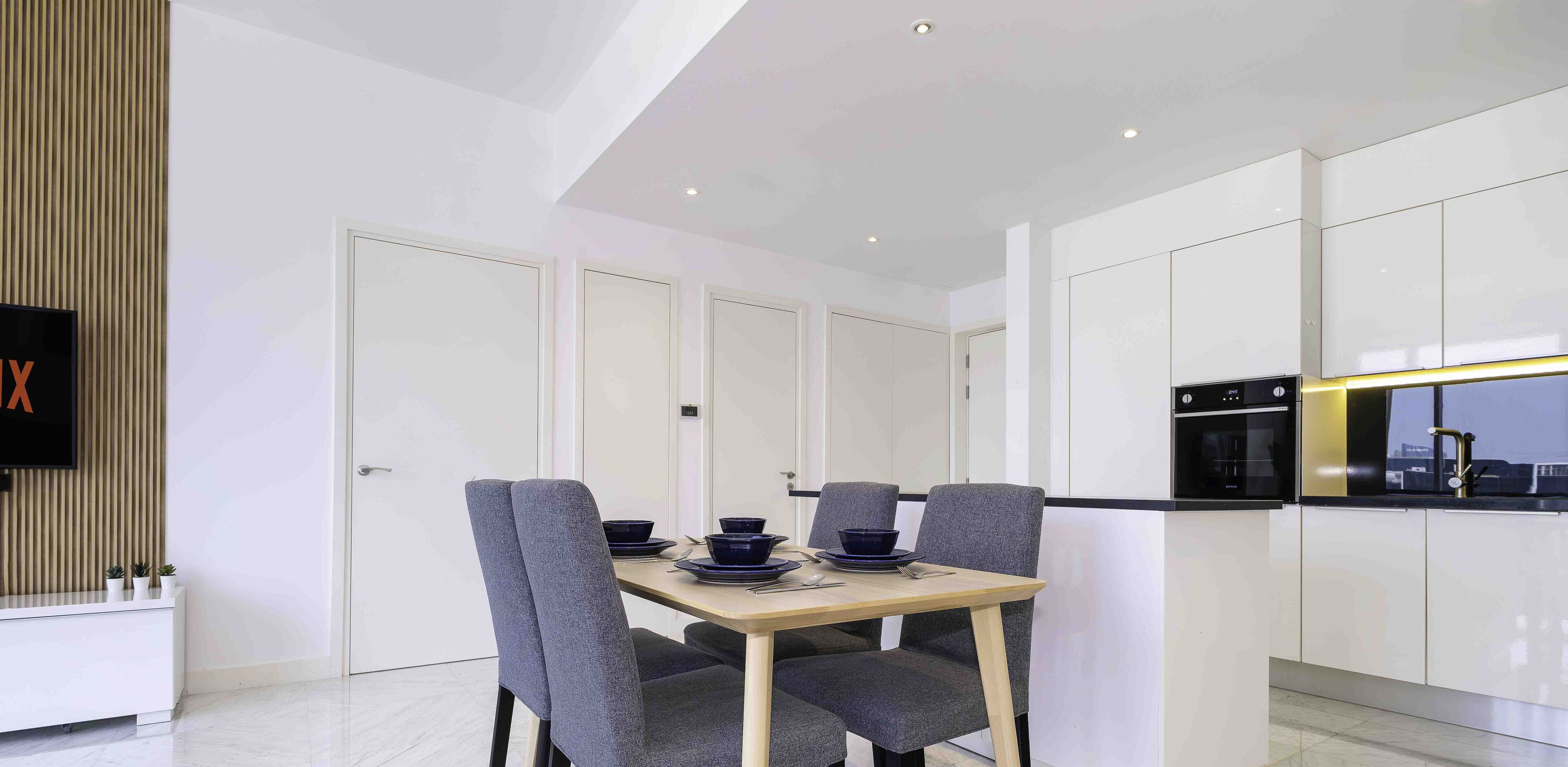 Un espace repas moderne avec une table en bois, des chaises à revêtement gris et un téléviseur fixé sur un mur recouvert de panneaux en bois.