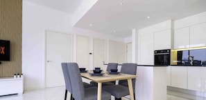 A modern dining area with a wooden table, grey upholstered chairs, and a TV mounted on a wooden panel wall.