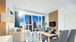 A modern hotel room with a city view, a dining area, and a television displaying 'NETFLIX'. - LUX The Pad Executive Suite 2 (Dubai)
