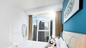 A modern hotel room with a large window offering a city view, a bed with patterned pillows, and a blue accent wall. - LUX The Pad Executive Suite 2 (Dubai)