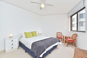 A bedroom with a bed, nightstands, a ceiling fan, a window, and wicker furniture.