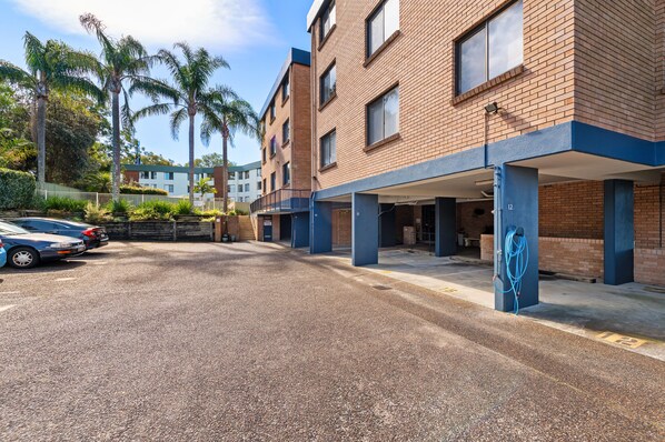 A parking area with a gravel surface, a covered carport, and a multi-story building with brick walls and blue accents.