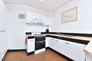 A compact kitchen with white cabinets, a stove, oven, and a sink.