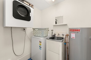 A compact laundry room with a washing machine, a dryer, a water heater, and a sink.