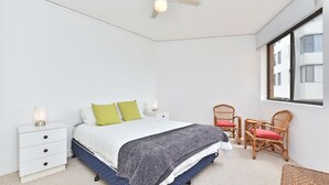 Ein Schlafzimmer mit einem Bett, zwei Nachttischen, einem Sessel und einem Fenster.
