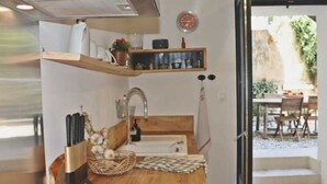 A compact kitchen with a wooden countertop, a sink, and a small window. There is a shelf above the sink with various items, and a door leading to a patio area. - The rose house (Buis-les-Baronnies)
