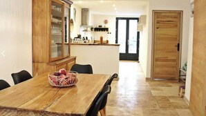 A dining area with a wooden table and chairs, a fruit basket, and a kitchen in the background. - The rose house (Buis-les-Baronnies)