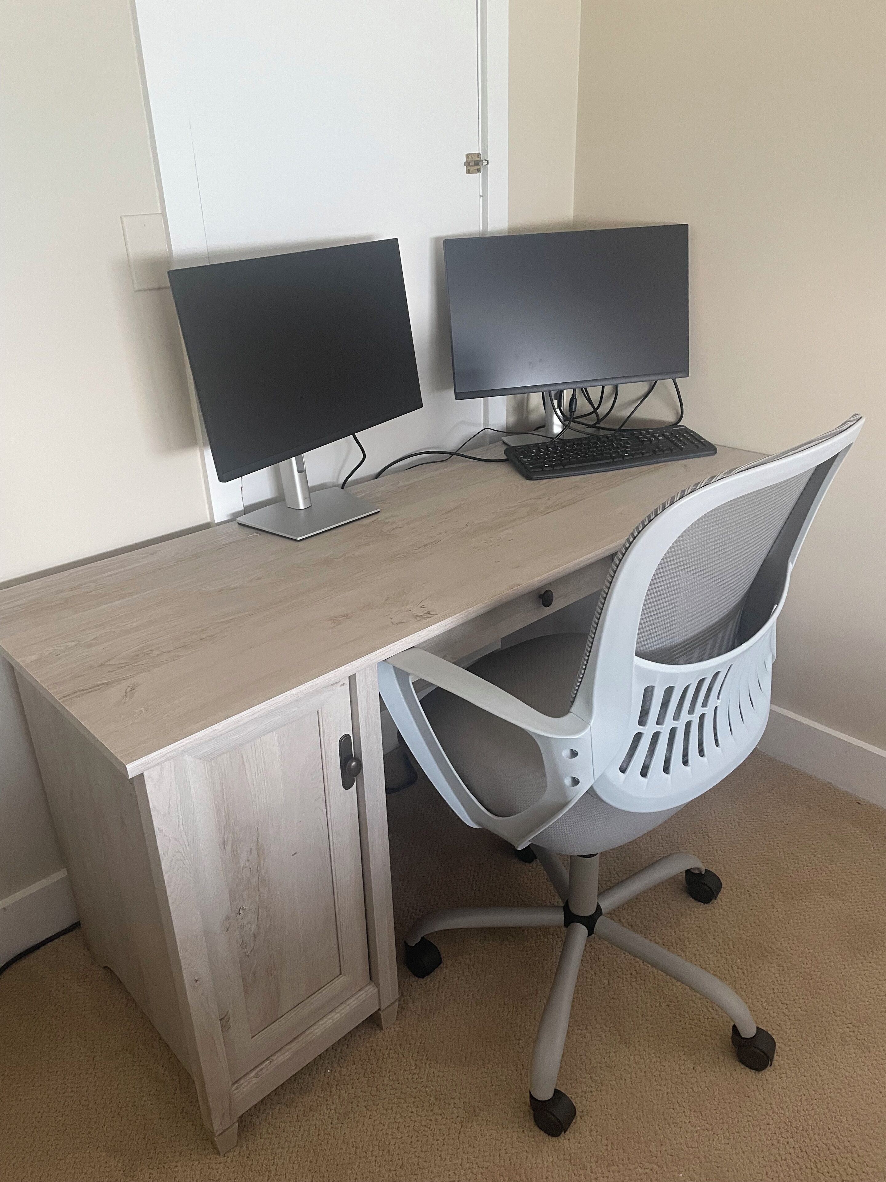 Un escritorio de madera con dos monitores, un teclado y una silla de oficina con respaldo de malla.